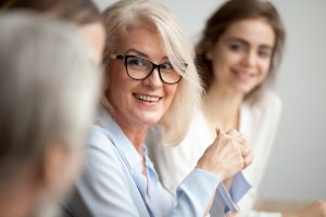 Smiling aged businesswoman looking listening to colleague at team meeting