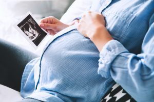 pregnant woman hands on belly holding ultrasound image